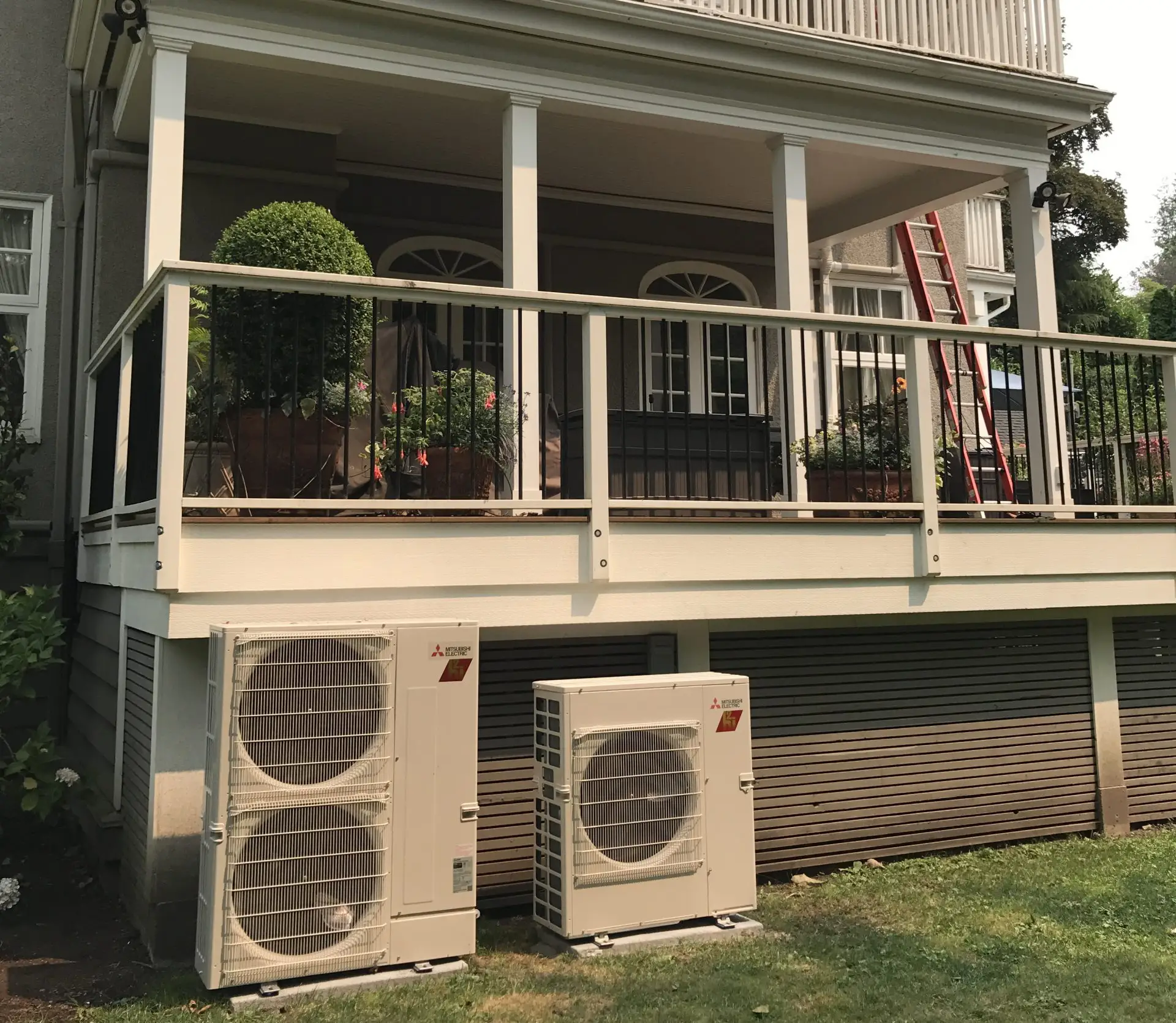 Two Mitsubishi Electric outdoor condenser units installed on concrete pads beneath a residential deck