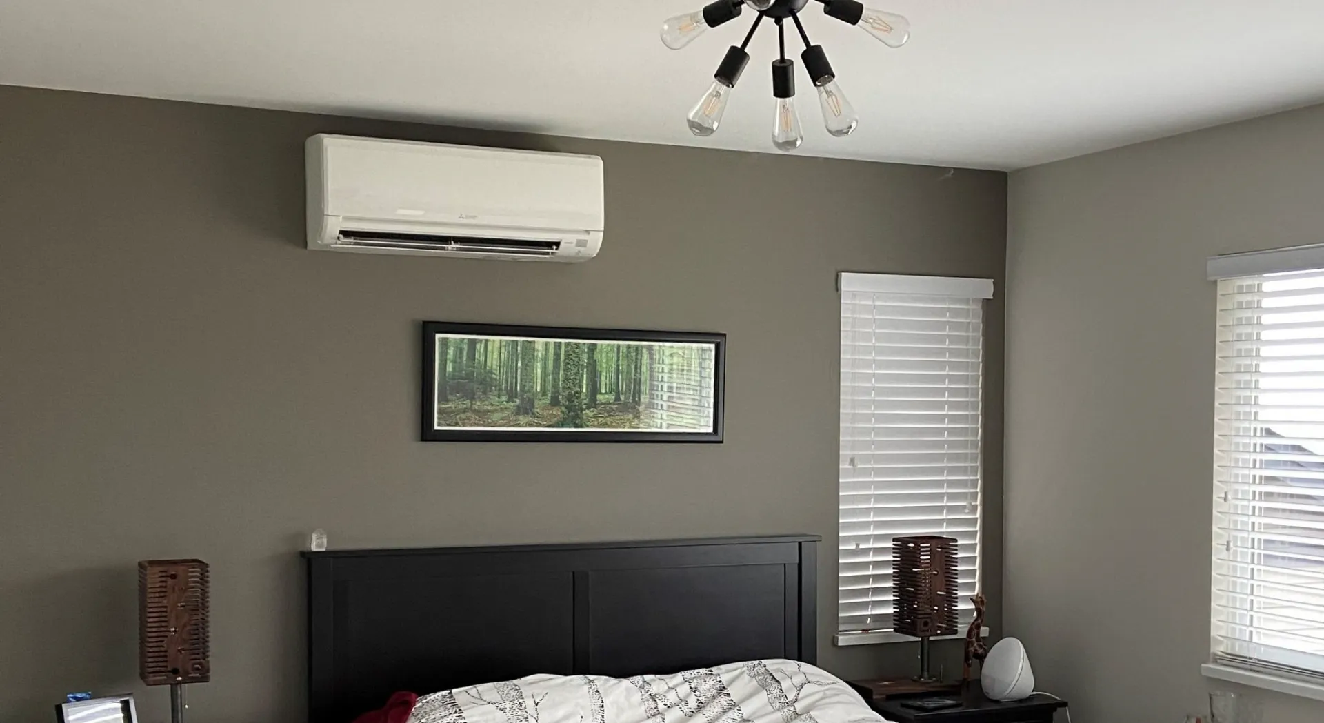 White Mitsubishi mini-split indoor unit mounted on grey bedroom wall above dark wood bed frame
