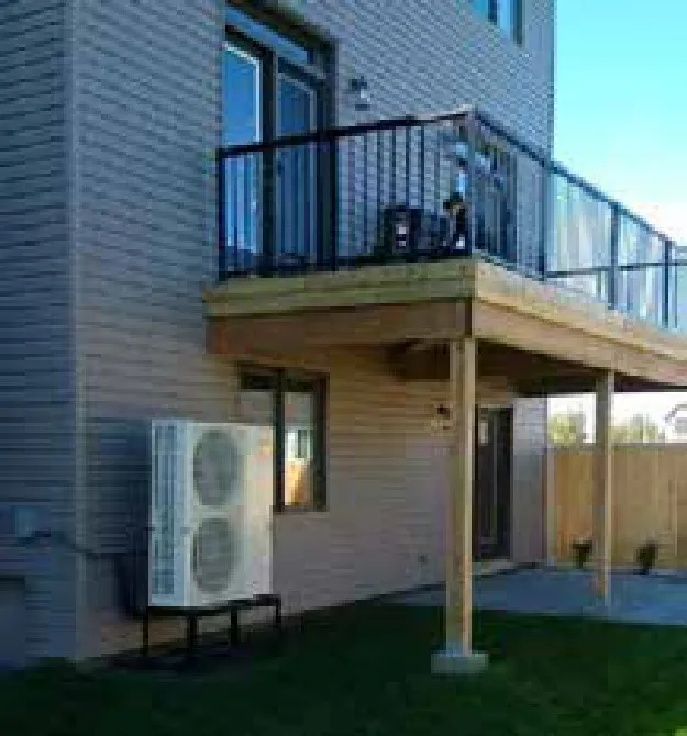 Exterior residential condenser unit mounted at grade beside multi-storey building with deck