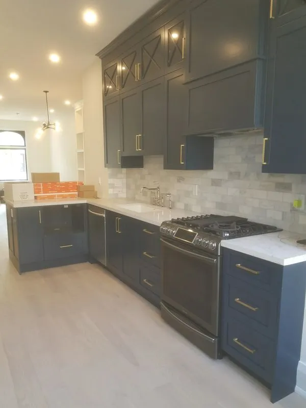 Dark navy shaker kitchen cabinets with gold hardware, white quartz countertops, marble tile backsplash, and stainless gas range during Oakville renovation
