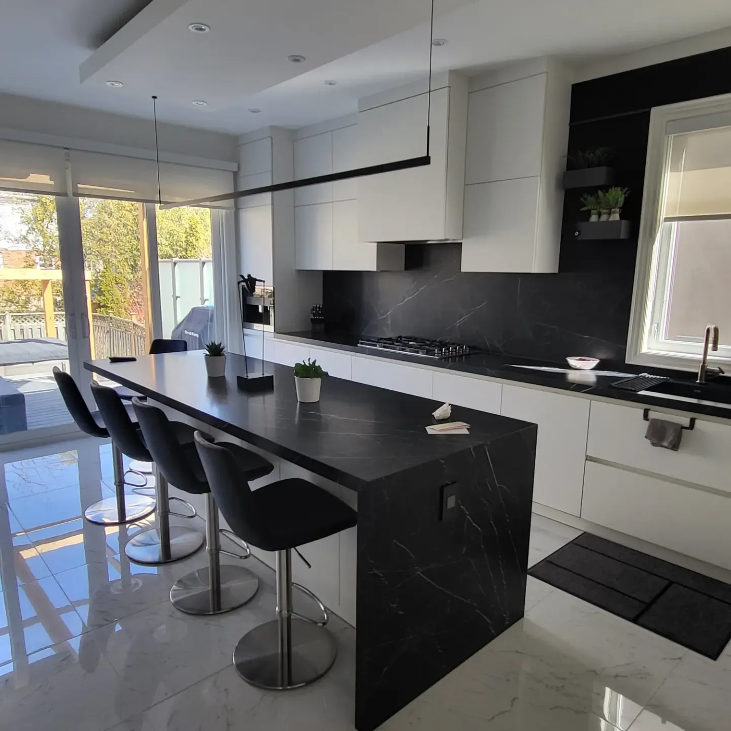 Bright Toronto kitchen renovation with black stone island, white handleless cabinets, and sliding glass door to backyard