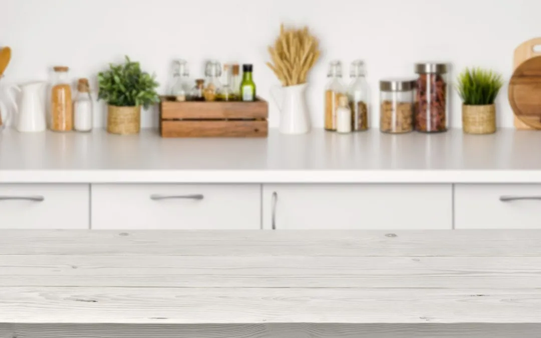 White kitchen counter and blurred cabinetry with jars and plants on shelves in background